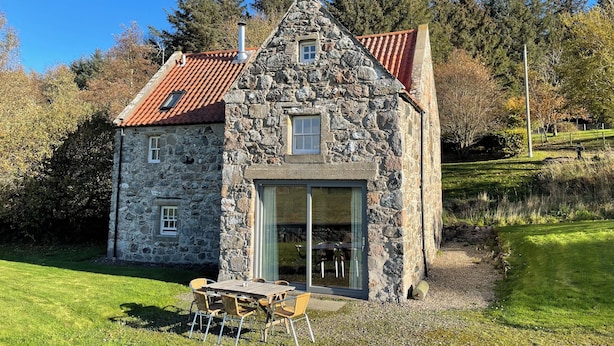 A stone house with a red-tiled roof, a glass door entrance, and a small outdoor table with chairs. - Beautiful Renovated Mill near Portsoy and the many beaches along the Moray Firth (Banff)