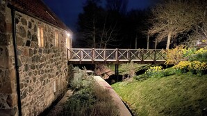 A stone building with a wooden bridge over a small stream, surrounded by greenery and flowers. - Beautiful Renovated Mill near Portsoy and the many beaches along the Moray Firth (Banff)
