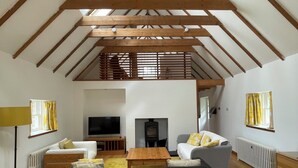 A loft-style room with exposed wooden beams, a sofa, a television, a fireplace, and a window with curtains. - Beautiful Renovated Mill near Portsoy and the many beaches along the Moray Firth (Banff)