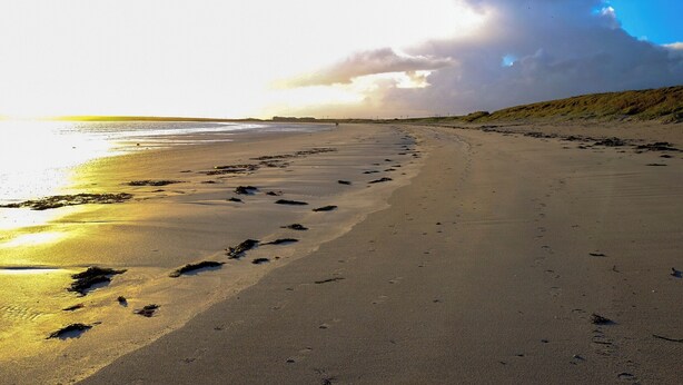 Ein weiter Sandstrand mit Fußspuren und Seetang, der zum Wasser führt.