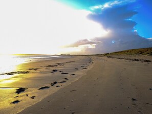 A wide sandy beach with footprints and seaweed, leading to the water. - Mingro is a unique beachside cottage that serves as a retreat from modern life. (Stronsay, near Whitehall)