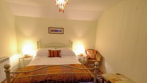 Ein Einzelbett mit Metallgestell, zwei Nachttische mit Lampen, ein Sessel und ein Bild an der Wand.