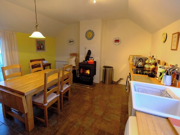 A cozy living room with a fireplace, wooden dining table, and chairs. - Mingro is a unique beachside cottage that serves as a retreat from modern life. (Stronsay, near Whitehall)