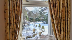 Une fenêtre donnant sur un jardin enneigé, avec des rideaux et deux pichets blancs en céramique posés sur le rebord de la fenêtre.