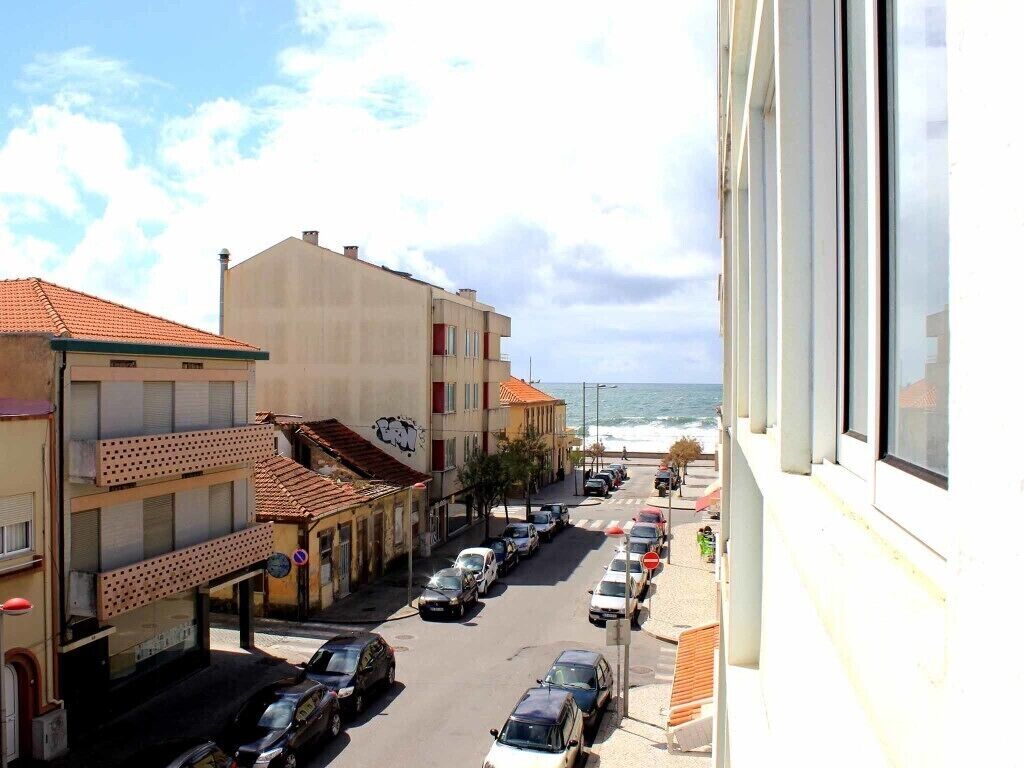 Eine Küstenstraße mit parkenden Autos, Gebäuden mit roten Ziegeldächern und Blick auf das Meer.