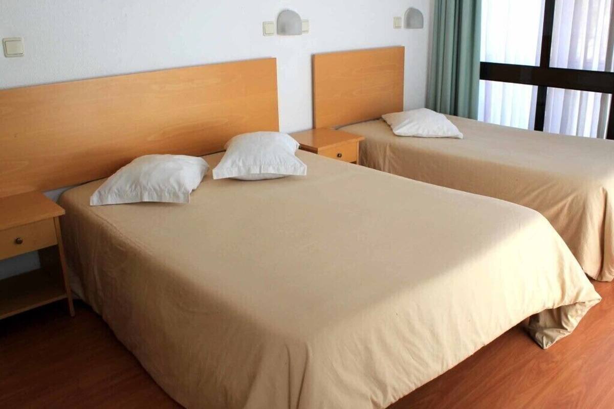 A hotel room with two beds, each with a wooden headboard and beige bedding.