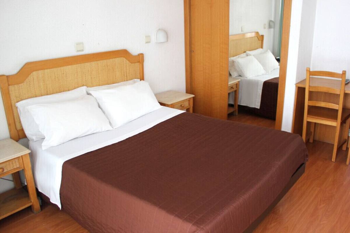 A hotel room with a large bed, a wooden nightstand, a chair, and a mirror.