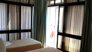 Quarto de hotel com duas camas, uma janela grande com cortinas e vista para o exterior.