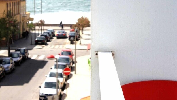 Vista da rua com carros estacionados, faixa de pedestres e um edifício com telhado vermelho.