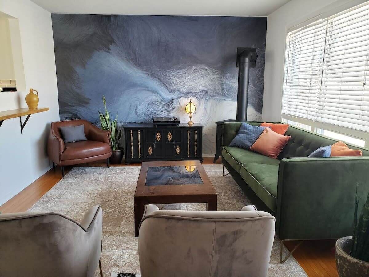 A living room with a large abstract mural, a green sofa, a brown leather armchair, and a coffee table.