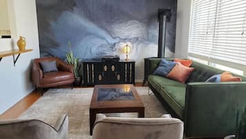 A living room with a large abstract mural, a green sofa, a brown leather armchair, and a coffee table.