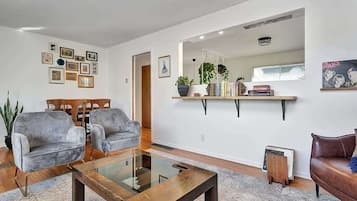 A modern living room with a glass coffee table, grey sofas, a brown leather sofa, and a bookshelf with decorative items.