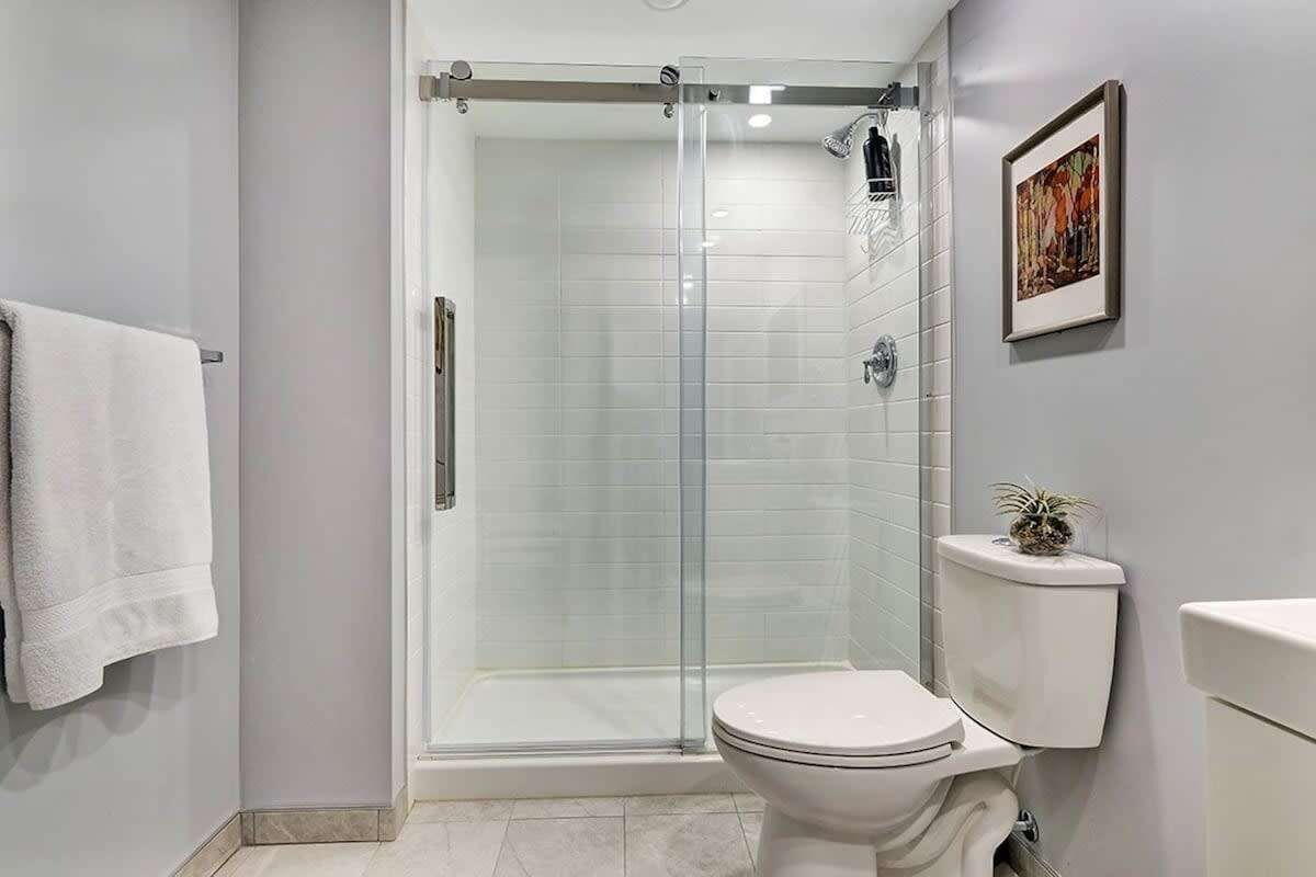 Un baño moderno con ducha de vidrio, inodoro blanco y una obra de arte enmarcada en la pared.