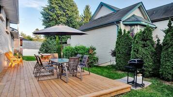 A wooden deck with a table and chairs, a barbecue grill, and a covered patio area.