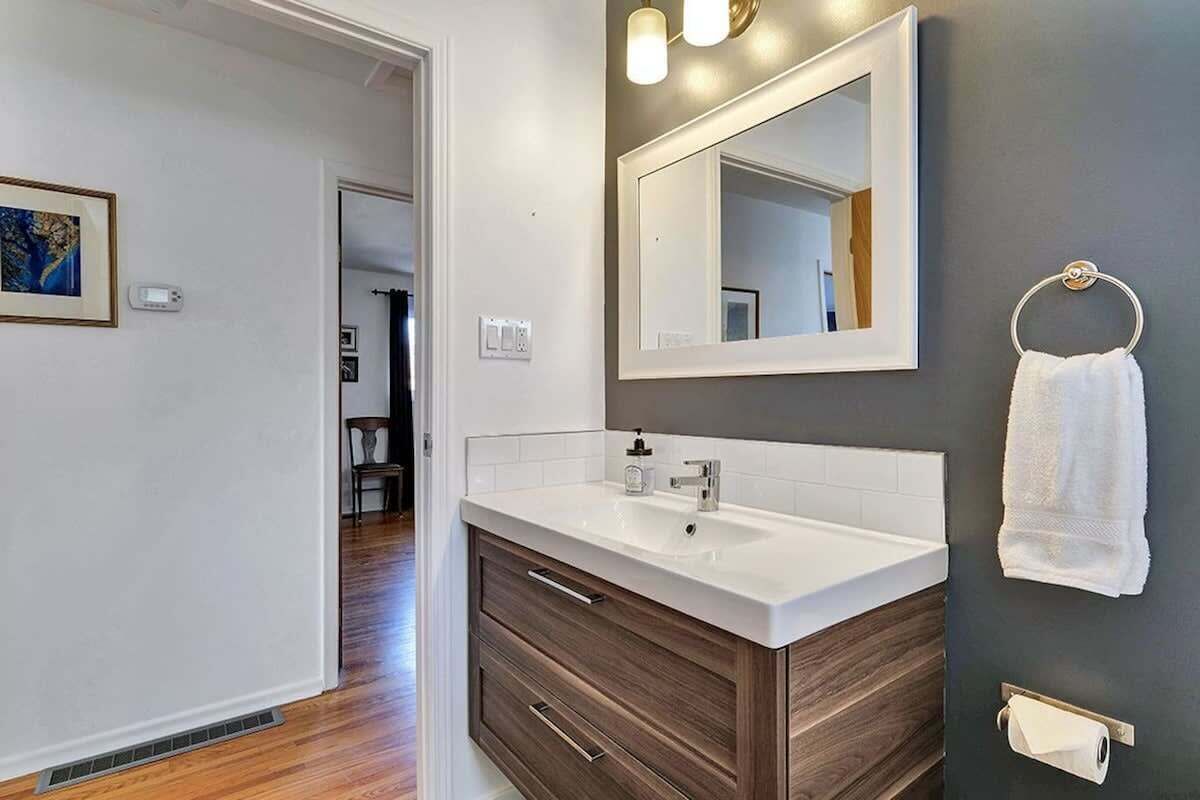 A modern bathroom with a white vanity, a large mirror, and a towel ring on the wall.