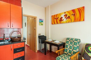 A compact room with a kitchenette, a dining area with a table and chairs, and a colorful painting on the wall.
