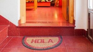 A hotel entrance with a red carpet, a doormat with 'HELLO' written on it, and a colorful sofa in the background.