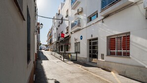 A narrow urban street with buildings on either side, a pedestrian walkway, and a clear sky.