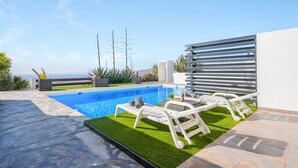 Una piscina con sillones de descanso, vista al mar y un espacio exterior moderno con pérgola.