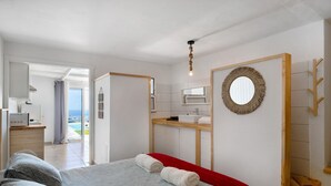 Habitación de hotel con cama, una manta roja, un espejo redondo, una escalera de madera y vista al océano.