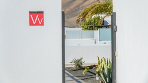 Un edificio blanco con un letrero rojo que dice 'Vv' y una montaña al fondo.