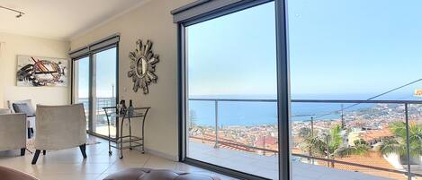 A spacious living room with a large sliding glass door leading to a balcony with a city view.