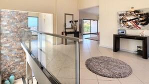 A spacious living area with a glass railing, a stone wall, a large abstract painting, and a modern console table. - Villa Moniz - Four Bedroom House, Sleeps 8 (Funchal)