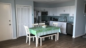 A compact kitchen with white cabinets, a dining table with four chairs, a refrigerator, a stove, and a dishwasher. - CORAL SURF B-1 - OCEANFRONT 2 BR AND 2 BATH CONDO (Carolina Beach)