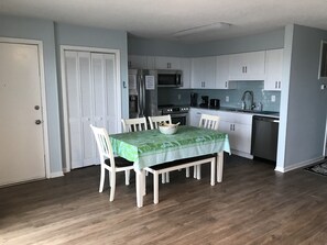 A compact kitchen with white cabinets, a dining table with four chairs, a refrigerator, a stove, and a dishwasher.