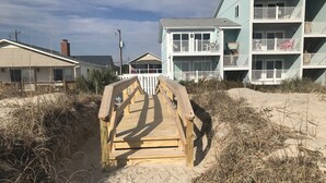 A wooden boardwalk leading to a beachfront property with a two-story building featuring balconies. - CORAL SURF B-1 - OCEANFRONT 2 BR AND 2 BATH CONDO (Carolina Beach)