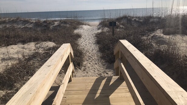 A wooden boardwalk leading to the beach with sand and sparse vegetation. - CORAL SURF B-1 - OCEANFRONT 2 BR AND 2 BATH CONDO (Carolina Beach)
