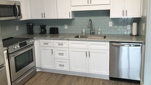 A modern kitchen with white cabinets, a stainless steel dishwasher, a built-in oven, a microwave, and a coffee maker. - CORAL SURF B-1 - OCEANFRONT 2 BR AND 2 BATH CONDO (Carolina Beach)