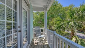 A covered porch with a wooden deck, a metal chair, and a table. - Dreamscaper - Five Bedroom, Four 1/2 Bath Home with private pool (Surfside Beach)