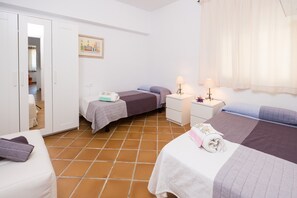 Un dormitorio con dos camas, un armario blanco, una mesita de noche con lámpara y un cuadro en la pared.