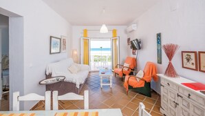 A room with a bed, a table, a chair, a TV, and a view of the sea.