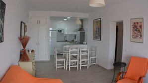 A modern living room with a dining area, white furniture, and a kitchen in the background.