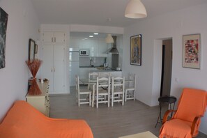 A modern living room with a dining area, white furniture, and a kitchen in the background.