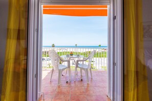 Un balcón con una mesa y sillas blancas, vista al mar y una cortina amarilla.