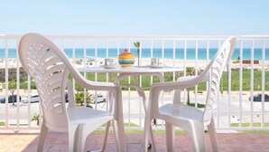 A balcony with white plastic chairs and a table, overlooking a beach and ocean.