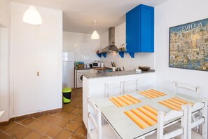 A compact kitchen with white cabinets, a blue accent wall, a dining area with a glass table, and a cityscape poster.