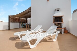 A rooftop with lounge chairs, a barbecue grill, and a covered seating area.