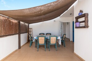 A covered patio with a table and chairs, a wooden ladder, and a wall-mounted shelf with potted plants.