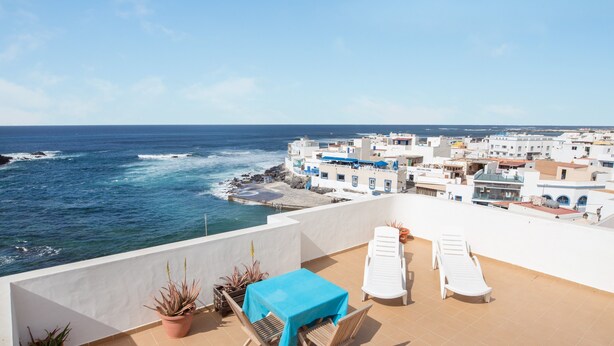 A terrace with a table and chairs, overlooking a coastal town and the sea.