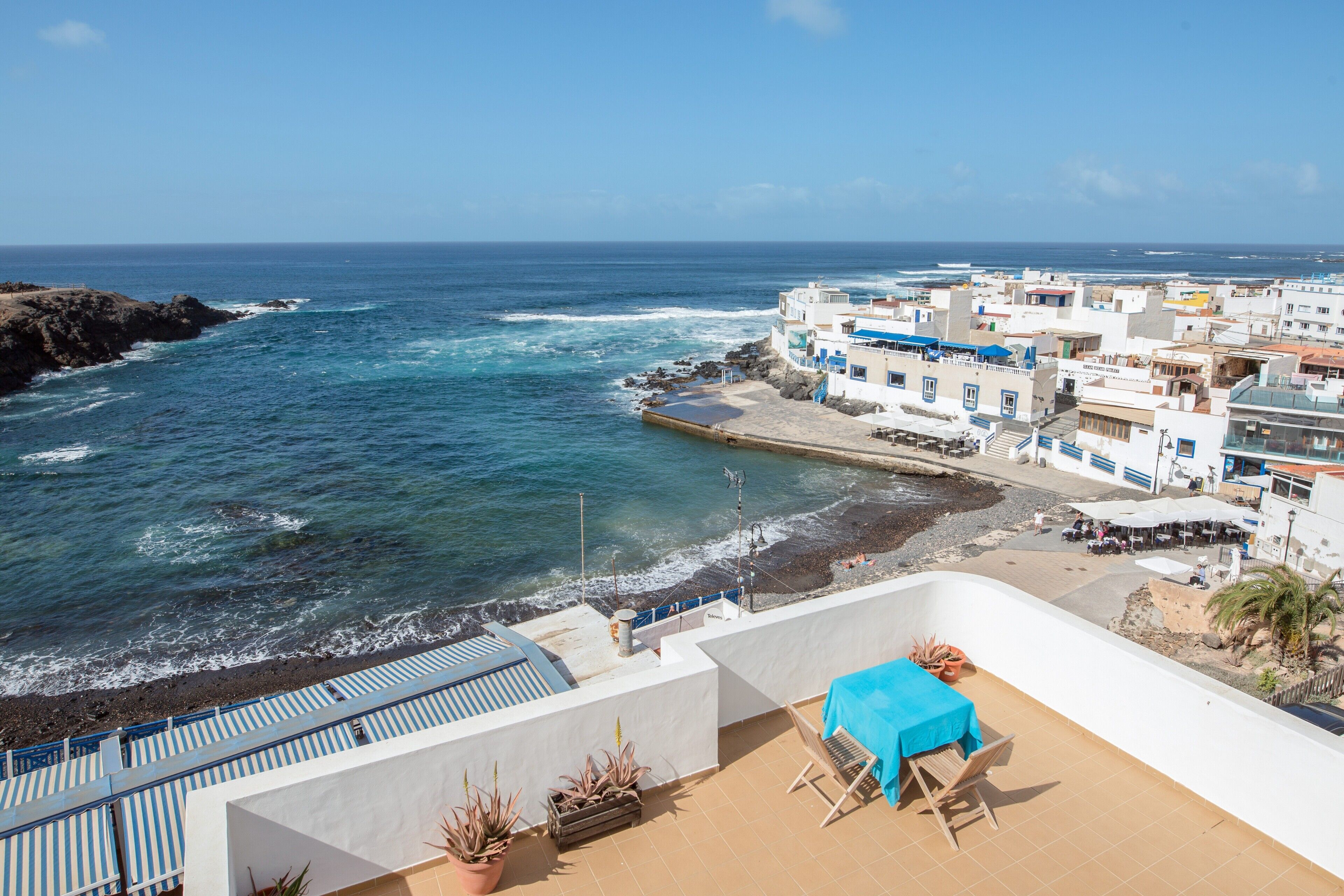 Ein Hotel an der Küste mit einer Terrasse mit Blick aufs Meer, einem Essbereich und Ausblick auf den Strand und den Ozean.