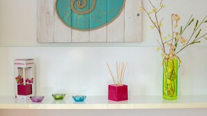 A shelf with a teal spiral decoration, a pink box, a green vase with branches, and a small blue bowl.