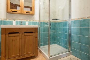 A bathroom with a wooden vanity, a glass shower enclosure, and blue-tiled walls.