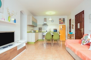 A compact living space with a kitchenette, a dining area with chairs, a sofa, a television, and a refrigerator. - Central Apartment "El Muellito" On the Beach with Rooftop Terrace & Wi-Fi (El Cotillo)