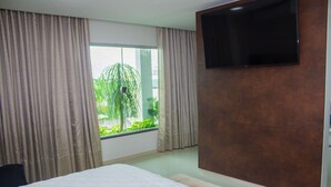 Ett hotellrum med en stor säng, en platt-TV som är monterad på väggen och ett fönster med gardiner.