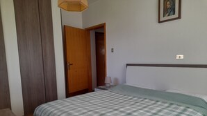 Une chambre à coucher comprenant un lit, une armoire en bois, une porte, une table de chevet avec une lampe et un luminaire fixé au mur.