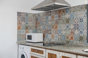 A kitchen with a washing machine, a microwave, and a tiled backsplash.